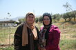 Two women stand in a field and smile at the camera