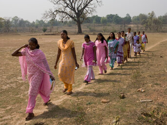 Women walking in a straight line across a dry field.