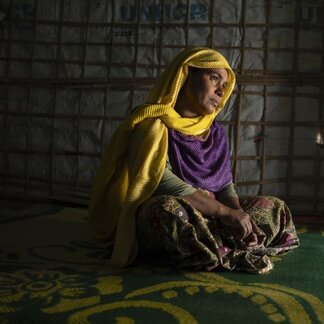 Rohingya refugee woman in  yellow headscarf sits on the floor in a tent in Bangladesh