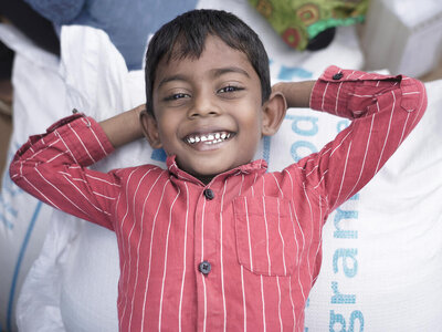 A young smiley boy lays on a rice bag with his hands resting on the back of his head.