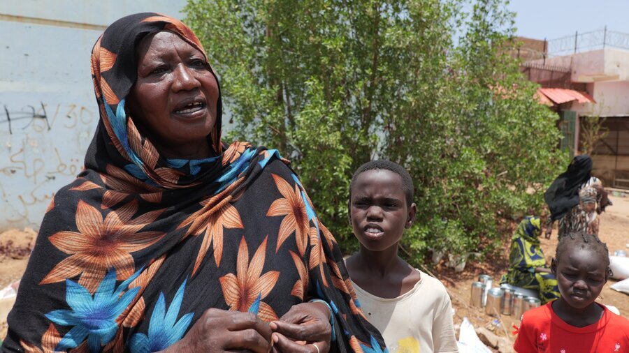 A woman in a black patterned headscarf and worried expression, stands next to two children in Khartoum, Sudan. Photo: WFP/Jonathan Dumont